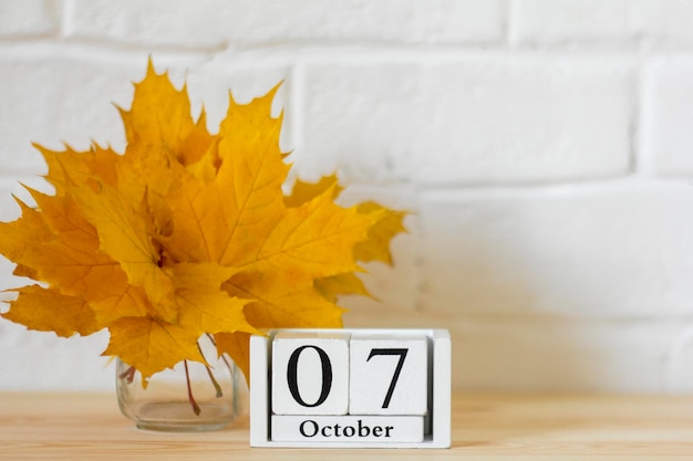 7 ottobre sul calendario e un mazzo di foglie autunnali luminose sul tavolo. Uno dei giorni del mese autunnale. Calendario per ottobre. Il concetto dell'autunno dorato.