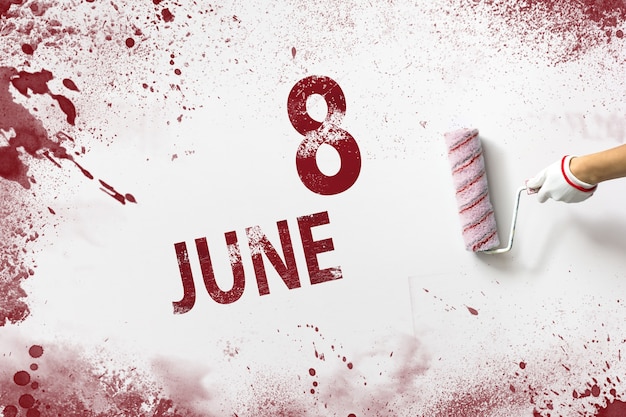 8 giugno. Giorno 8 del mese, data del calendario. La mano tiene un rullo con vernice rossa e scrive una data di calendario su uno sfondo bianco. Mese estivo, concetto di giorno dell'anno.