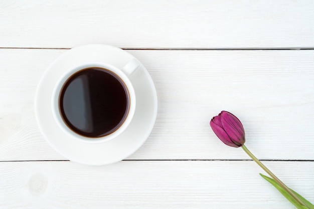 8 marzo, un tulipano e una tazza di caffè su uno sfondo di legno chiaro.