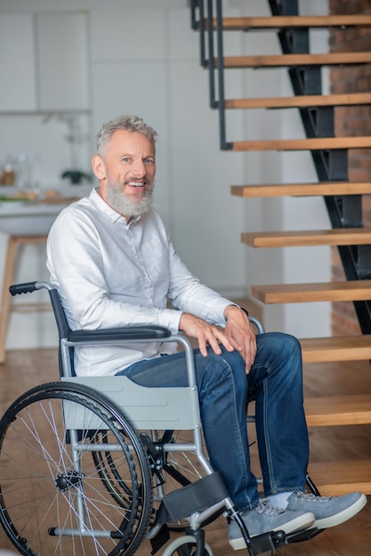 A casa. Uomo disabile dai capelli grigi in camicia bianca e jeans a casa