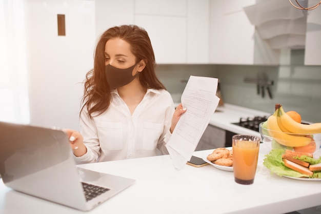 A causa della pandemia di coronavirus, una donna isolata in casa. Lavora a casa, indossa una maschera e tiene una videoconferenza sul suo laptop.