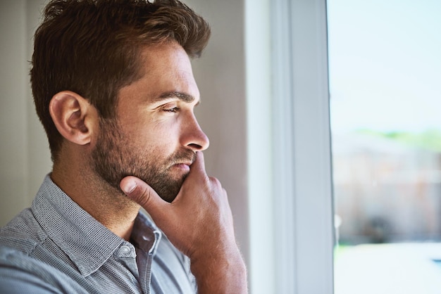 A cosa può pensare Inquadratura di un giovane concentrato che guarda attraverso una finestra mentre contempla l'interno a casa durante il giorno