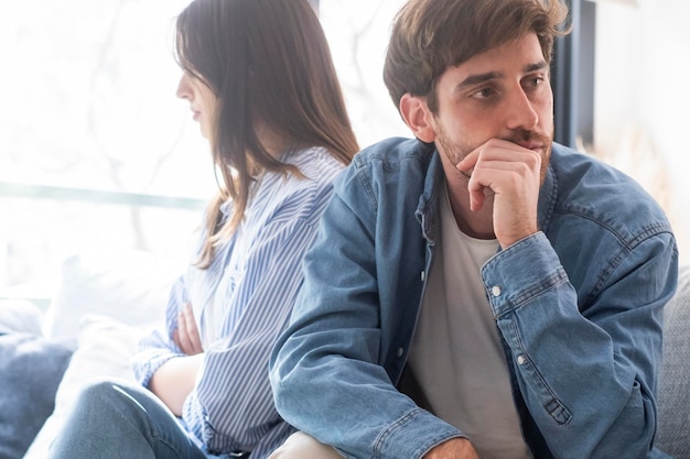 A couple in silence during a difficult moment in their relationship sitting apart on the couch with the wife pregnant and the husband deeply concerned Emotional tension
