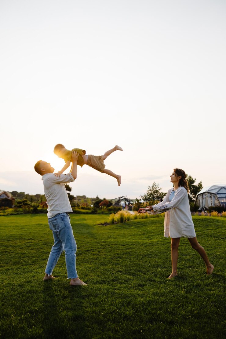 A Father Joyfully Tossing His Son in the Air as the Sun Sets Over a Beautiful Green Field