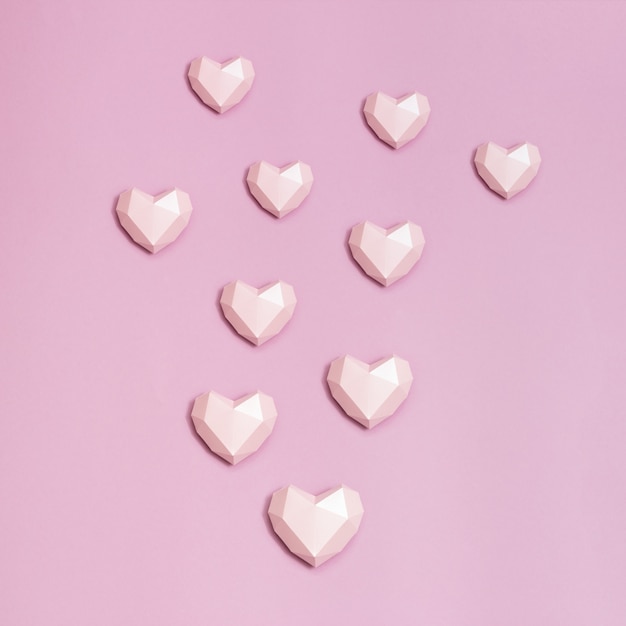A forma di cuore di carta poligonale rosa su carta rosa. Sfondo vacanza con copia spazio per San Valentino. Concetto di amore.