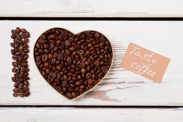 A forma di cuore e lettera I disposti con semi di caffè. Gustoso concetto di caffè. Plance di legno bianche.