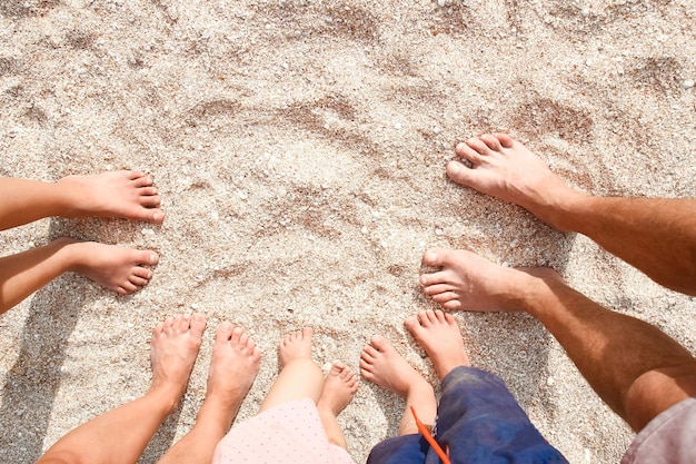 A Gambe della bella famiglia intera sulla sabbia vicino allo sfondo del mare