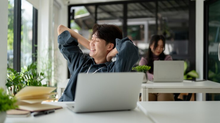 Photo a happy asian businessman is leaning back in his chair putting his hands behind his head