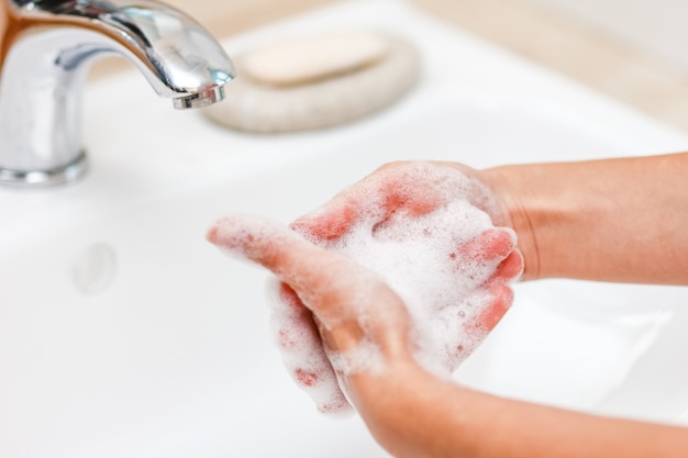 A Lavarsi le mani con sapone sotto il rubinetto con acqua