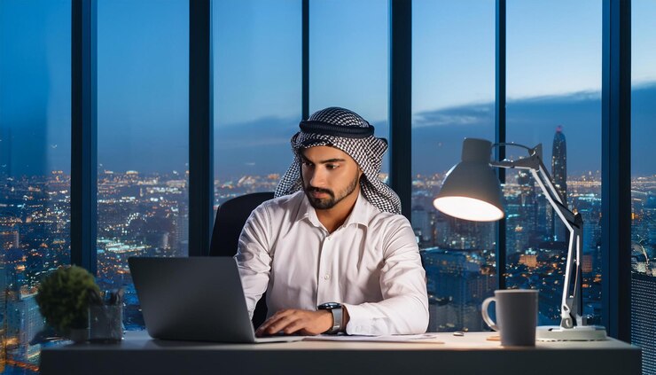 a man sits at a desk with a laptop and a coffee cup in front of him