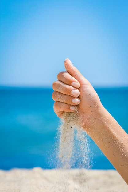 A Mani versano sabbia dal mare sulla natura in un viaggio. Vacanze in mare il tempo della sabbia passa.