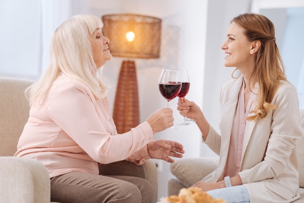 A noi. Donne piacevoli felici positive che si siedono uno di fronte all'altro e sorridono mentre i vetri tintinnanti