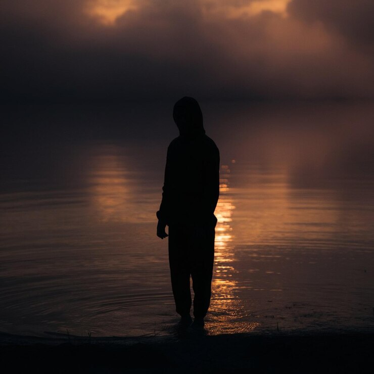a person stands in the water with the sun behind their head
