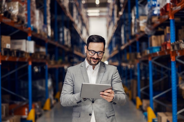 A warehouse worker is adding orders and tracking goods while scrolling and smiling at tablet