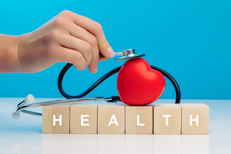 A woman's hand holds a stethoscope and touches a red heart that lies on top of wooden cubes with the inscription HEALTH