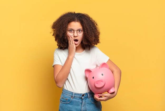 Abbastanza adolescente afro che scrolla le spalle, si sente confuso e incerto, dubitando con le braccia incrociate e lo sguardo perplesso. concetto di risparmio