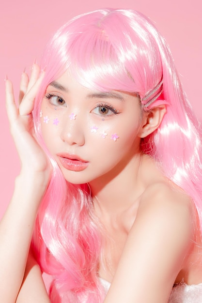 Abbastanza asiatica bella donna modello capelli lunghi con trucco fantasia sul viso e pelle perfetta accovacciata su sfondo rosa isolato Trattamento viso Cosmetologia chirurgia plastica