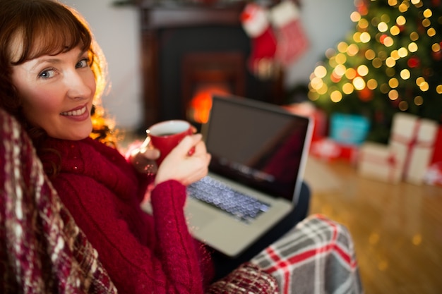 Abbastanza rossa che beve caffè e che utilizza computer portatile