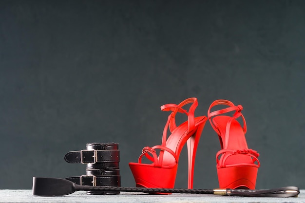 Abbigliamento BDSM per giochi sessuali per adulti Scarpe da striptease a tacchi alti rossi e manette frusta su immagine di sfondo scura