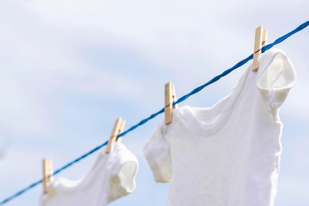 Abbigliamento bianco da bambino appeso a una corda all'aperto contro il cielo blu