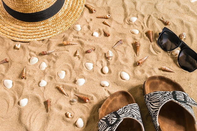 Abbigliamento mare estivo, infradito, cappello, occhiali da sole e conchiglie sulla spiaggia di sabbia