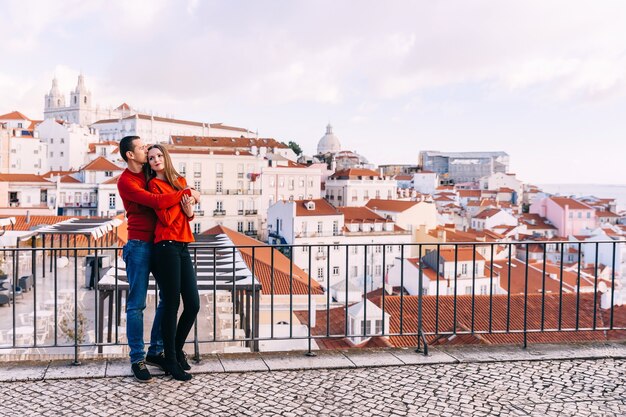 Abbracci romantici delle coppie in maglioni rossi sul fondo di panorama della città.