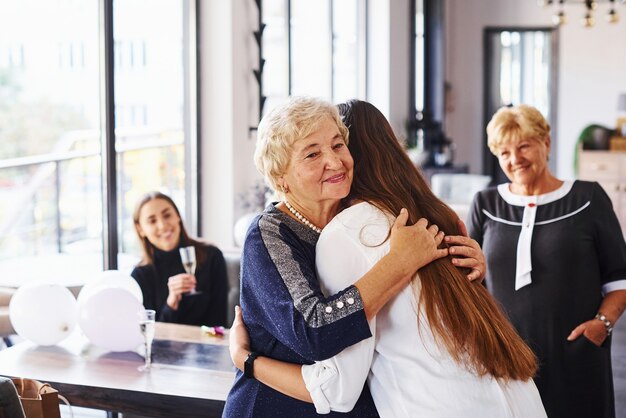 Abbracciandosi l'un l'altro. Senior donna con la famiglia e gli amici per festeggiare un compleanno al chiuso.