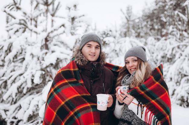 Abbracciare le coppie che guarda l'obbiettivo con sorrisi nella foresta nevosa di inverno