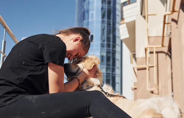 Abbracciarsi La giovane donna positiva si diverte con il suo cane quando fa una passeggiata all'aperto vicino all'edificio degli affari