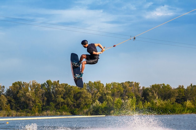 Abile wakeboarder maschio che salta con la rotazione della parte posteriore sull'acqua che tiene la corda in mano