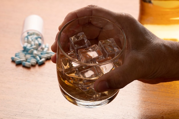 Abuso di alcol con un bicchiere di whisky con ghiaccio e pillole