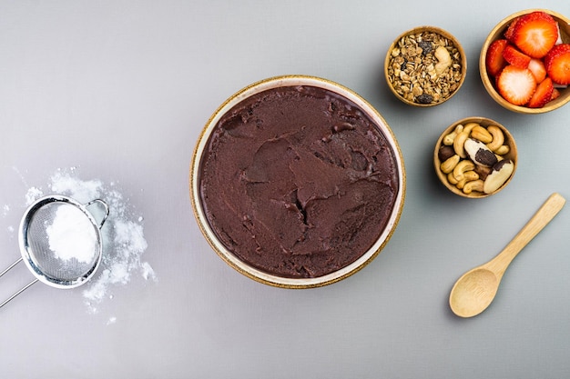 Acai brasiliano in una ciotola bianca granola alla fragola aggiuntiva e noci in piccole ciotole di bambù Anacardi e Para Vista dall'alto Sfondo grigio Messa a fuoco selettiva