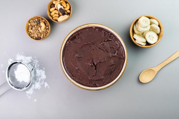 Acai brasiliano in una ciotola bianca granola di banana aggiuntiva e noci in piccole ciotole di bambù Anacardi e noci Para Vista dall'alto Sfondo grigio Messa a fuoco selettiva