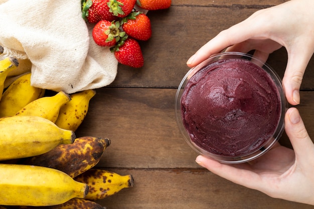 Acai, donna che tiene una ciotola di gelato alla bacca di Acai congelata brasiliana. con frutta sulla tavola di legno. Menu estivo vista dall'alto