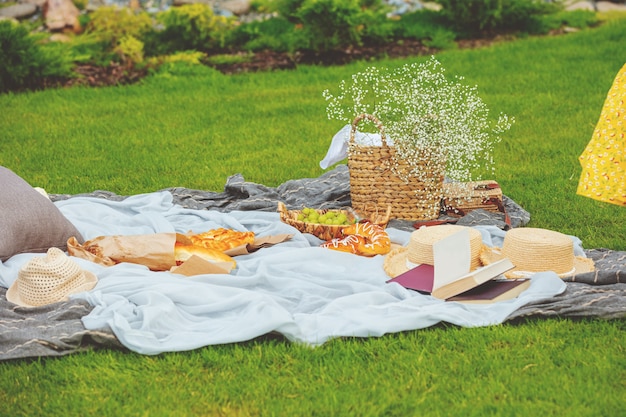 Accessori cappelli e cestino picnic sul prato su coperta con baguette croissant uva