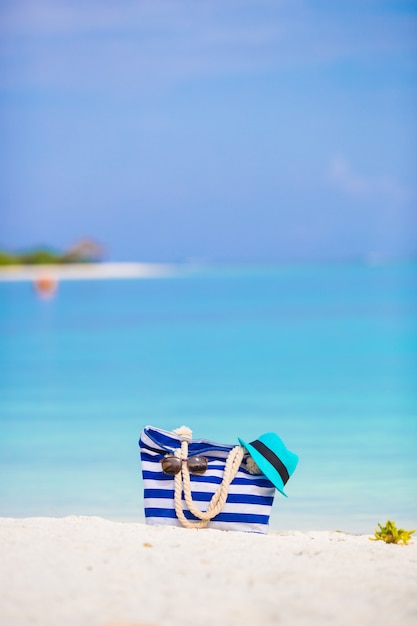 Accessori da spiaggia - borsa blu, cappello di paglia, occhiali da sole sulla spiaggia bianca