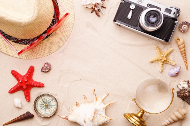 Accessori da spiaggia occhiali da sole cappello e fotocamera su sabbia con conchiglie e stella marina