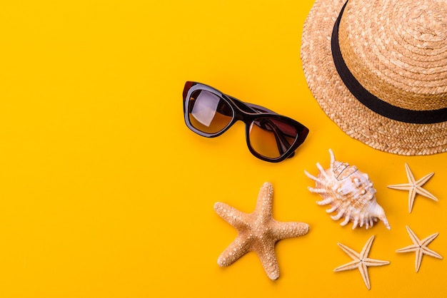 Accessori da spiaggia: occhiali e cappello con conchiglie e stelle marine su fondo colorato. Sfondo estivo