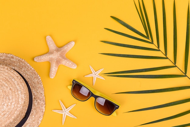 Accessori da spiaggia: occhiali e cappello con conchiglie e stelle marine su fondo colorato. Sfondo estivo