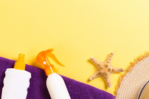 Accessori da spiaggia piatti laici con spazio di copia. Asciugamano blu e bianco viola, conchiglie, cappello da sole staw e una bottiglia di crema solare su sfondo giallo. Concetto di vacanza estiva