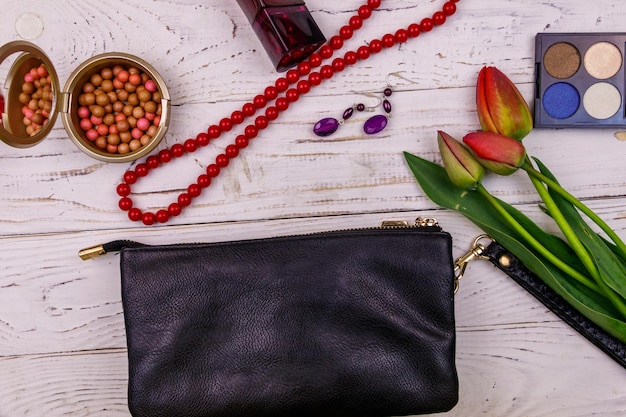 Accessori donna e cosmetici per il trucco su fondo di legno bianco Pochette profumo ombretto palline rosse collana orecchini e tulipani Composizione di bellezza e moda Vista dall'alto laici piatta