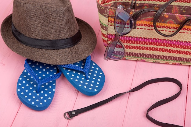 Accessori estivi occhiali da sole borsa da spiaggia in paglia cappello da sole cintura e infradito su tavolo in legno rosa