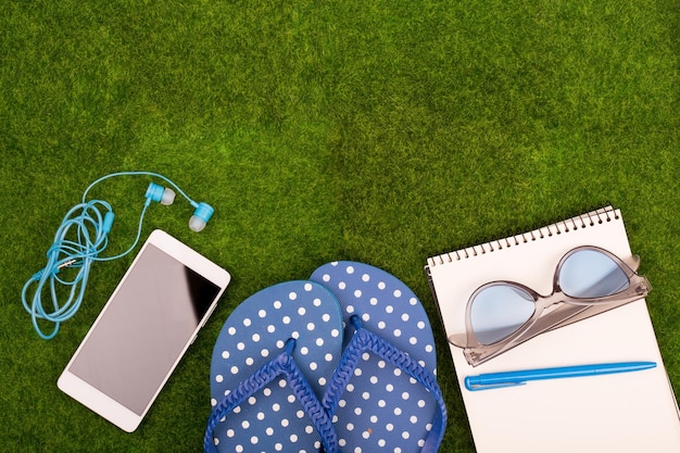 Accessori moda femminile infradito smart phone con cuffie note pad occhiali da sole sull'erba