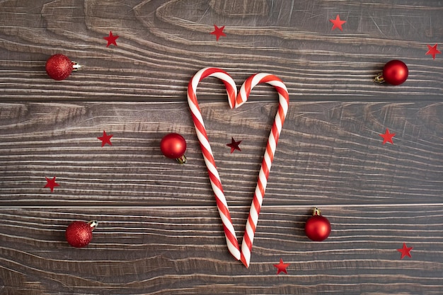 Accessori natalizi e cuore di caramelle lecca-lecca al centro su uno sfondo di legno scuro