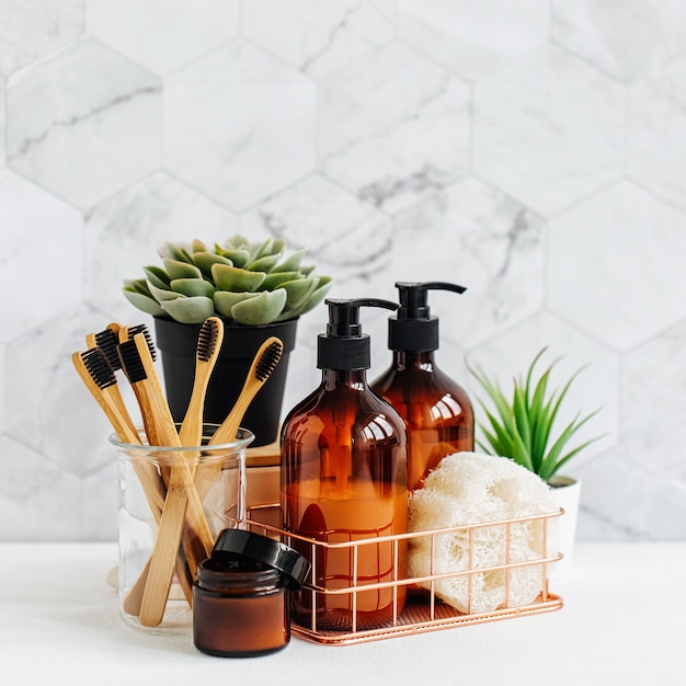 Accessori per il bagno, prodotti cosmetici naturali e strumenti con pianta verde sul tavolo bianco all'interno di uno sfondo del bagno.