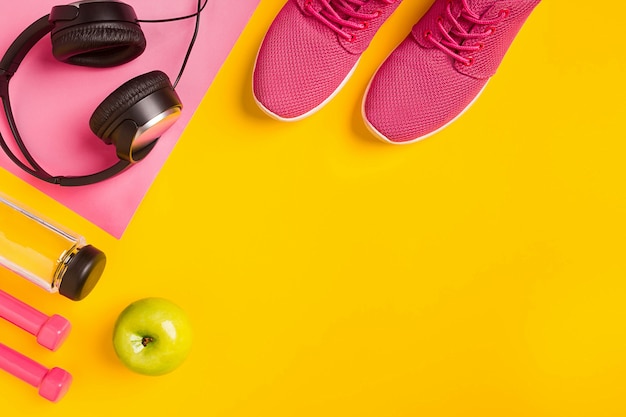 Accessori per il fitness su uno sfondo giallo sneakers bottiglia d'acqua auricolari e manubri