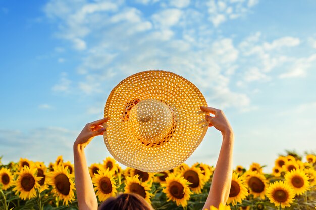 Accessori per le vacanze estive. La donna che cammina nel giacimento di girasole di fioritura ha sollevato il cappello su