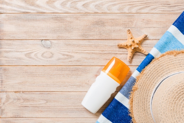 Accessori piatti da spiaggia con copia spazio. Asciugamano a strisce blu e bianco, conchiglie, cappello da sole staw e una bottiglia di crema solare su fondo di legno. Concetto di vacanza estiva.