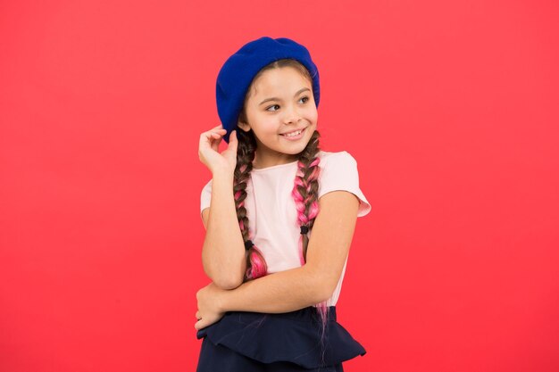 Accessorio berretto alla moda Moda adolescente Attributo di moda francese Bambino piccola ragazza bambino sorridente felice Bambino piccola ragazza di moda carina in posa con lunghe trecce e cappello sfondo rosso Ragazza di moda