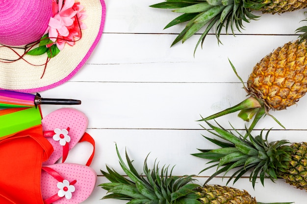 Accessorio da spiaggia, cappello, occhiali da sole, scarpe e ananas su legno bianco, viaggi vacanze estive e saldi estivi